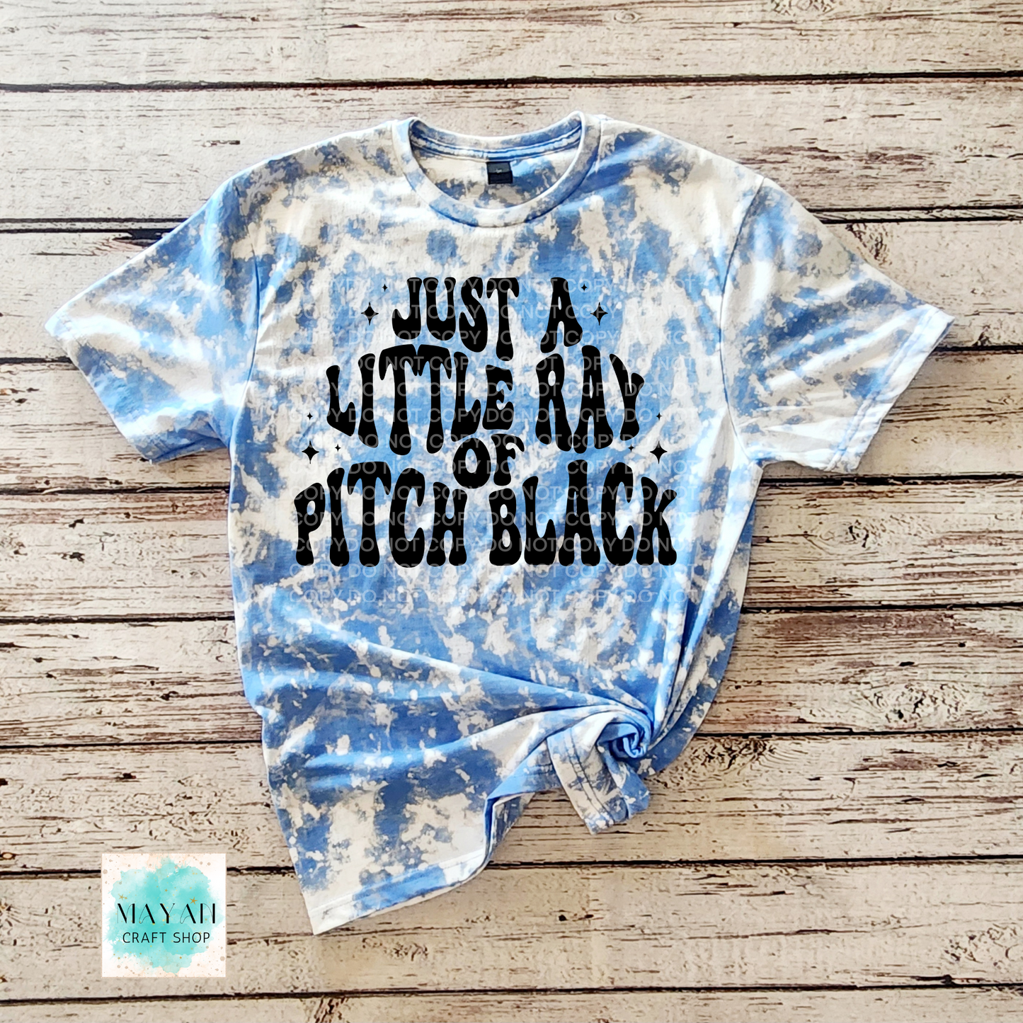 Tie-dye t-shirt with text on a wooden surface, featuring the brand "Mayan Craft Shop".