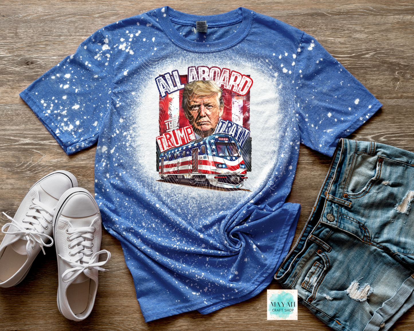 Blue t-shirt with graphic design featuring a face and text, displayed with white sneakers and jeans on a wooden surface.