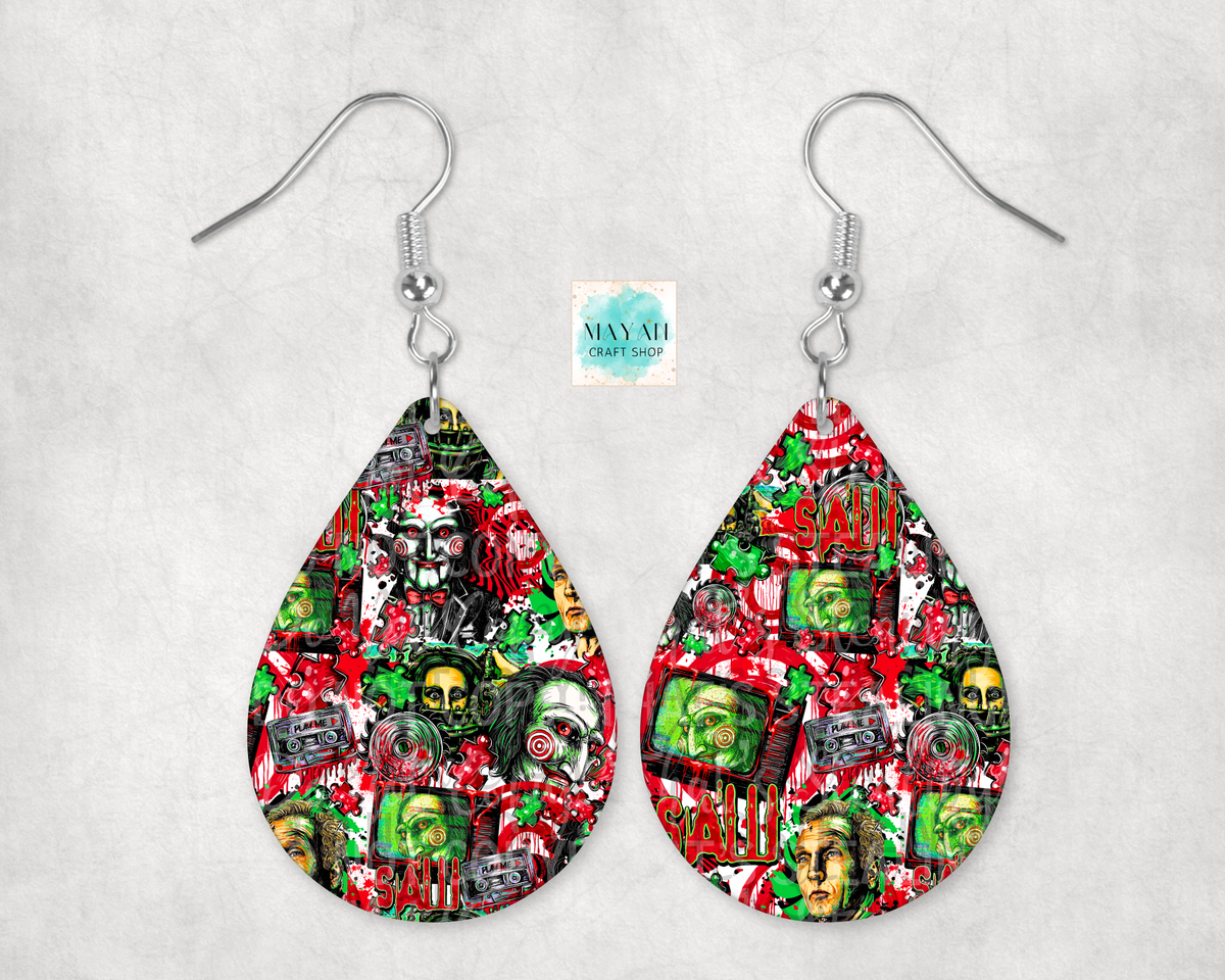 A pair of silver-tone dangle earrings with teardrop-shaped charms featuring a busy collage print in red, green, black, and white. The collage includes skulls, cassette tapes, and graffiti-style text.