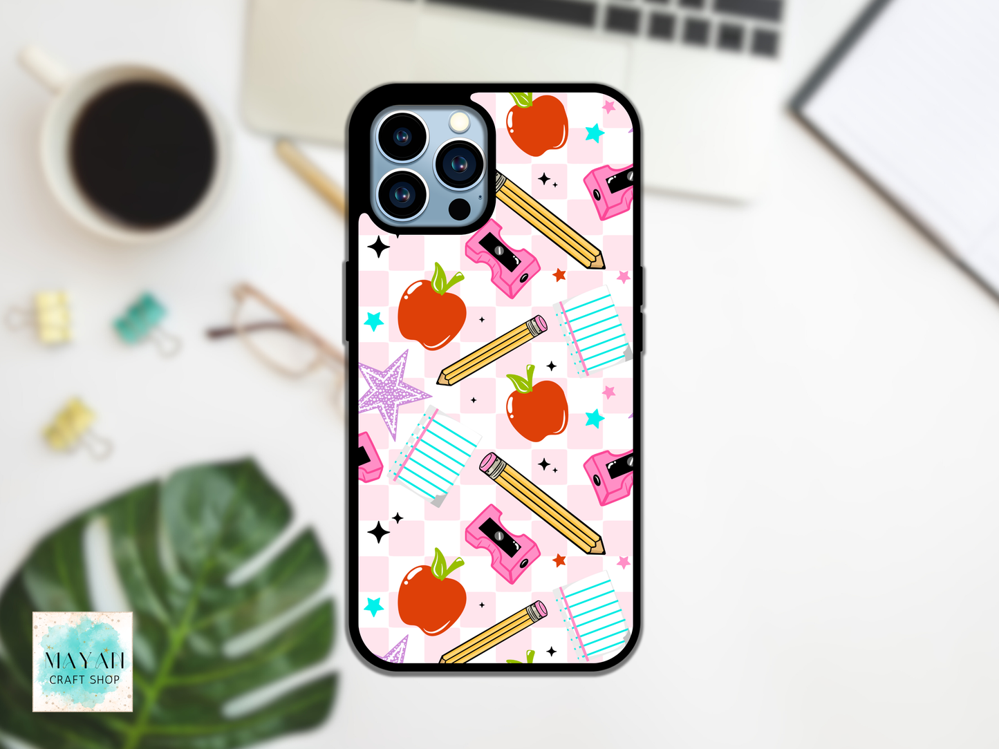 Phone case with school-themed design on a desk with a laptop and coffee cup.