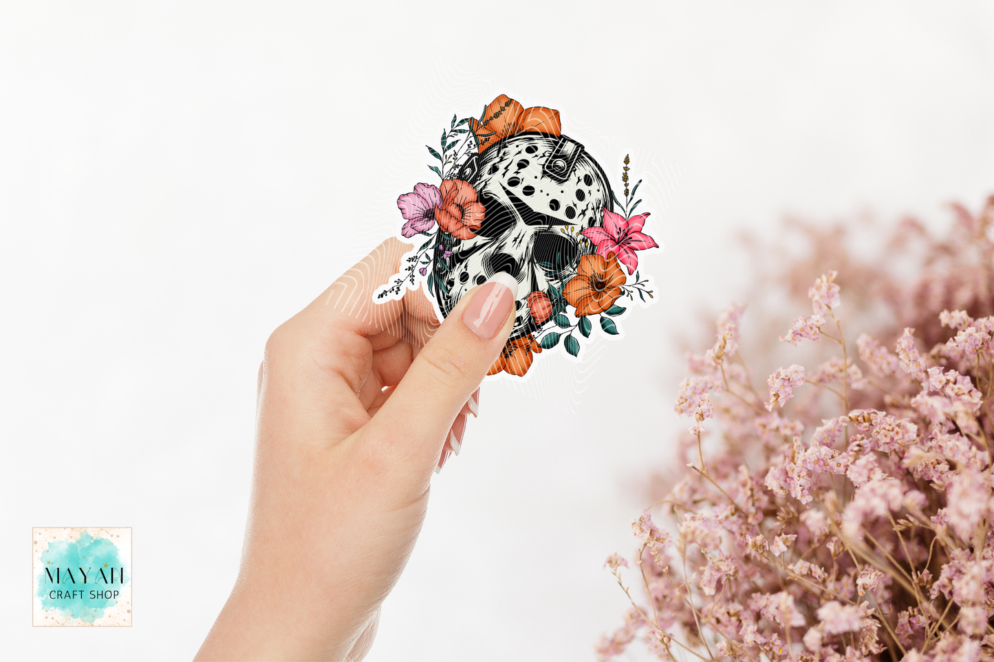 Hand holding a decorative mask with flowers against a white background