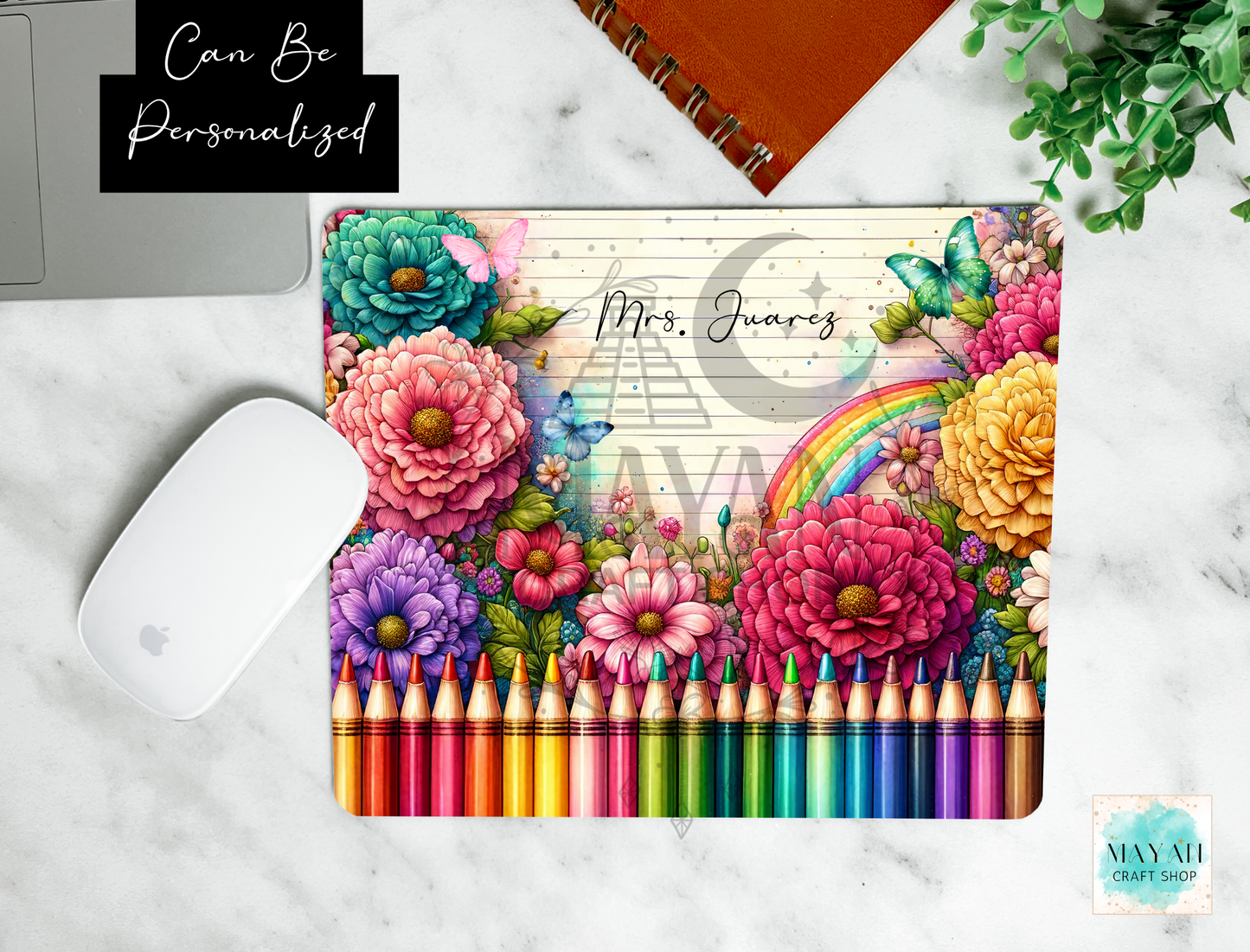 A personalized mouse pad featuring a colorful floral and rainbow design with 'Can Be Personalized' overlay, styled on a white marble surface with a white mouse, colored pencils, and a notebook.