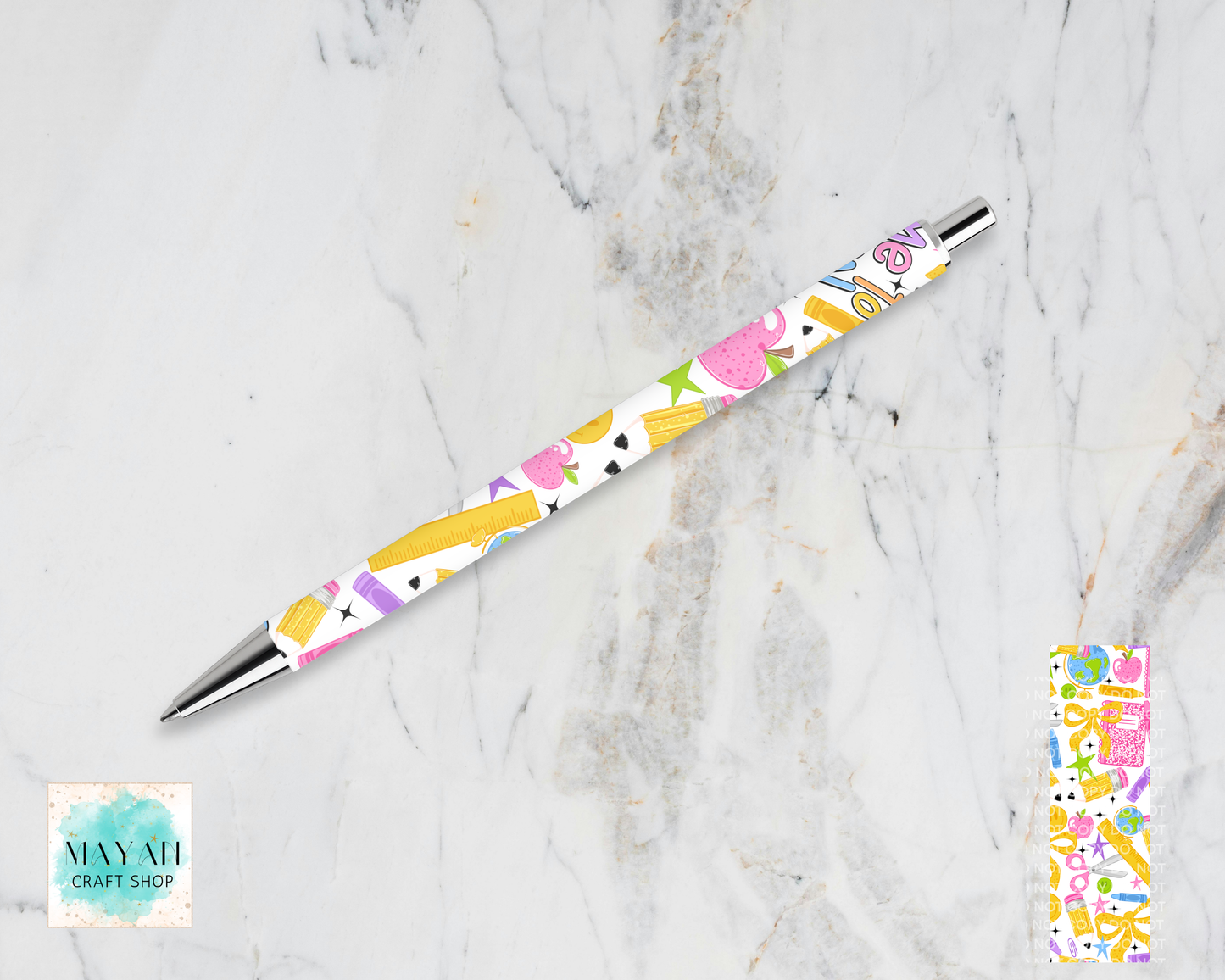 A retractable pen with a colorful pastel pattern of apples, rulers, and stars on a white background, resting on a light gray marble surface. A small inset of the patterned pen tip is shown in the bottom-right.