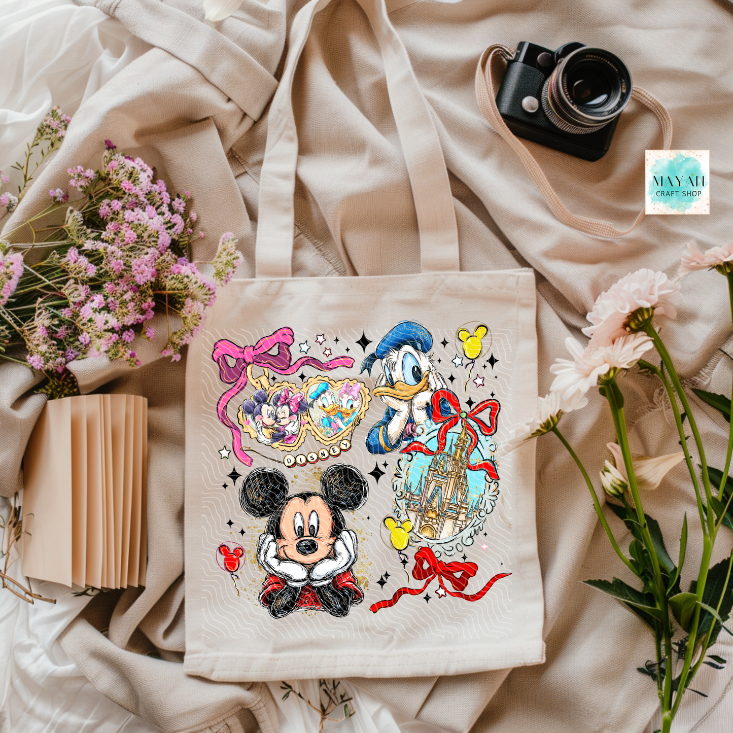 Tote bag with cartoon characters on a soft fabric background with flowers and a camera.