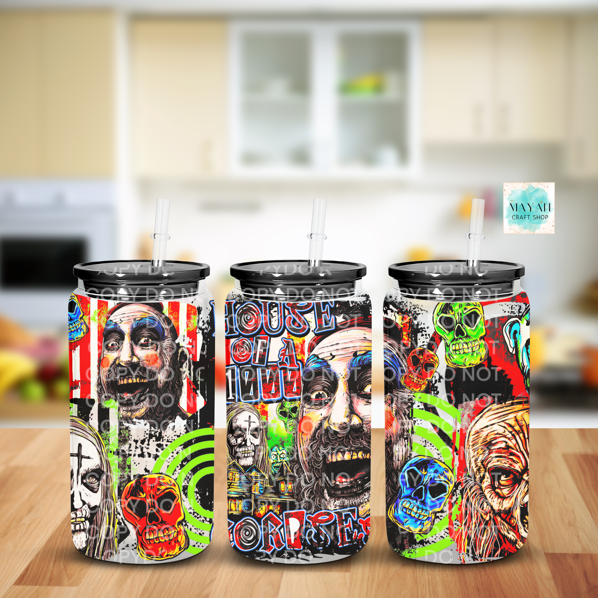 Three tall insulated tumblers with clear straws are shown on a wooden surface against a blurred kitchen background. The tumblers feature a vivid multicolor graphic print with skulls, faces, and text.