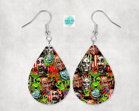 A pair of silver-tone dangle earrings with teardrop-shaped charms featuring a dense, colorful collage print of skulls, faces, and neon green spiral motifs on a black background, displayed against a light gray textured backdrop.