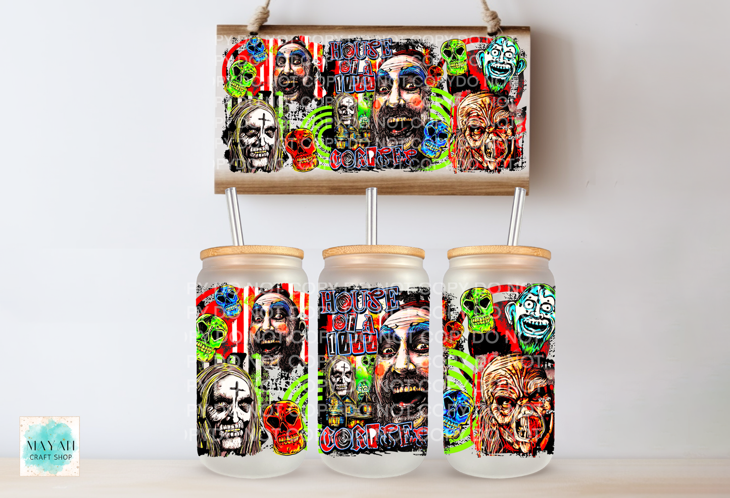 Three clear glass canisters with light wood lids and metal straws, decorated with a colorful horror-themed collage print, displayed below a matching rectangular sign on a light wall.