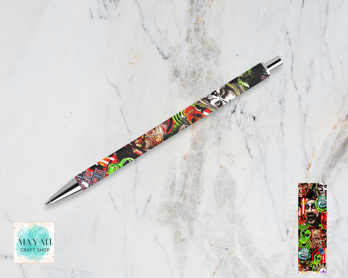A retractable pen with a colorful, busy graphic pattern on a black barrel, displayed diagonally on a white marble background.  A small inset image in the bottom-right shows the patterned end cap detail.