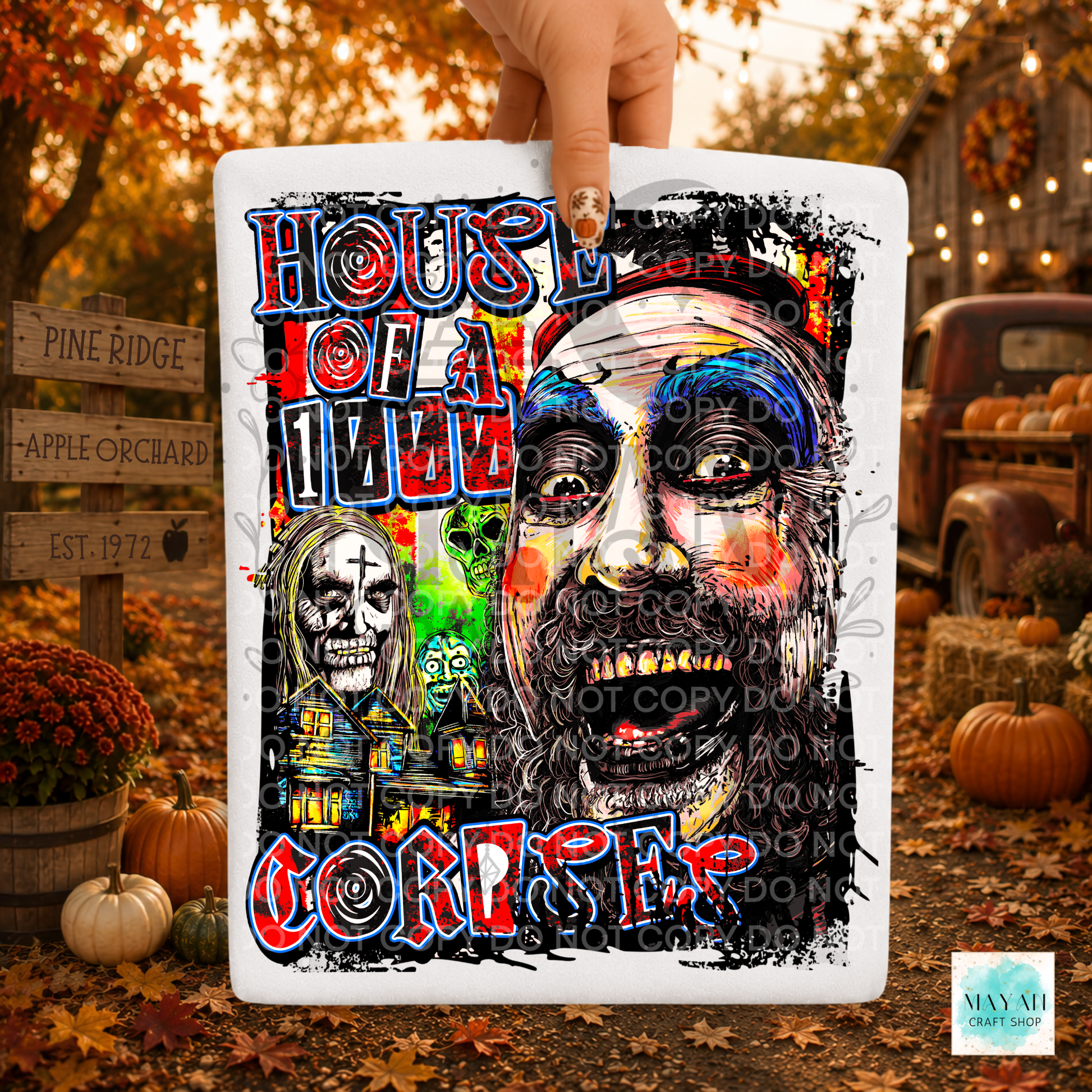 A rectangular white shirt featuring a colorful horror-themed graphic and illustrated faces, held by a hand against an autumn outdoor backdrop with pumpkins and fall foliage.