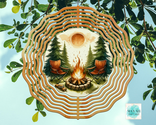 Decorative wind spinner with a campfire scene surrounded by trees, framed by natural elements.