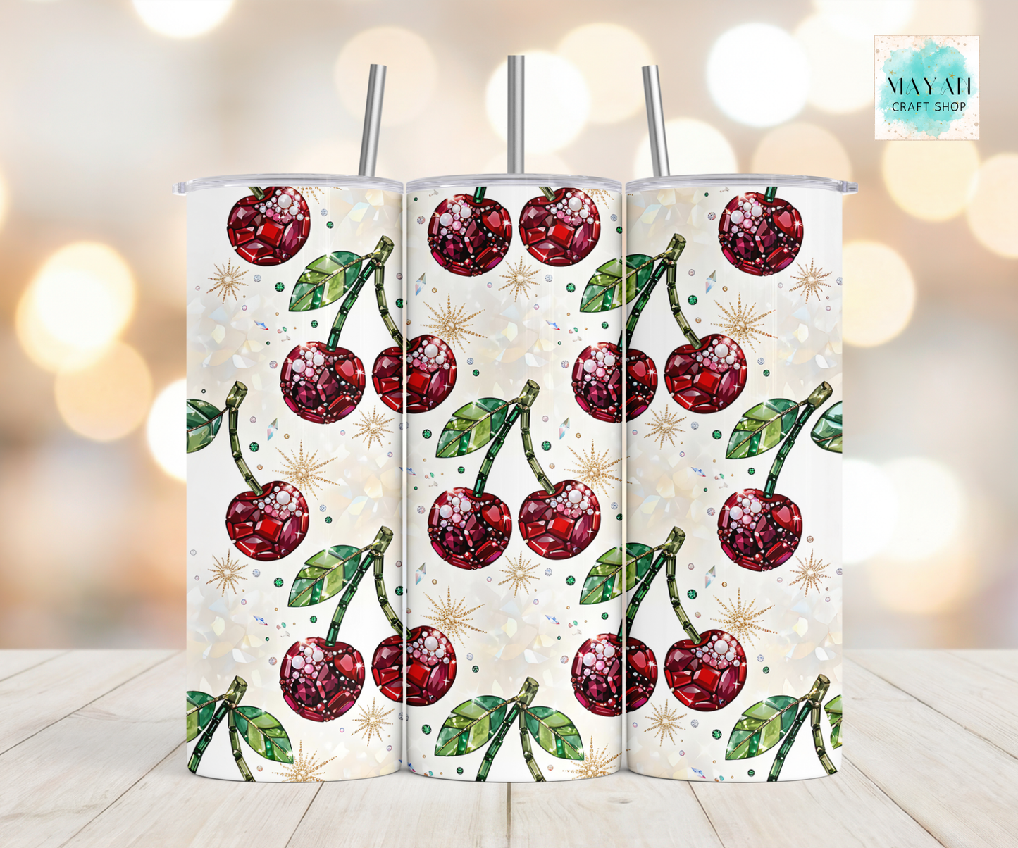 Three cherry-patterned tumblers on a light wooden surface with a blurred background.