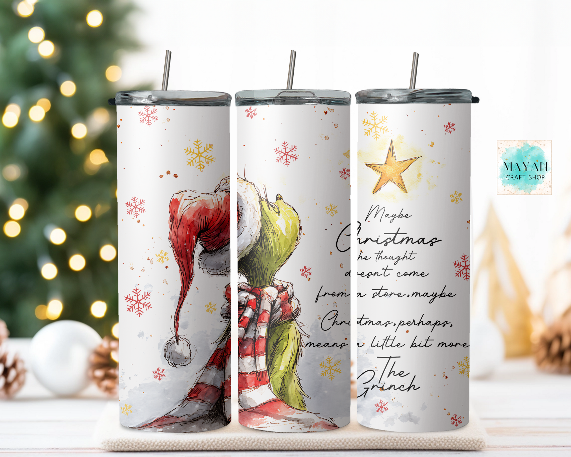 Three Christmas-themed tumblers with designs of a green character, and a quote on a blurred Christmas tree background.