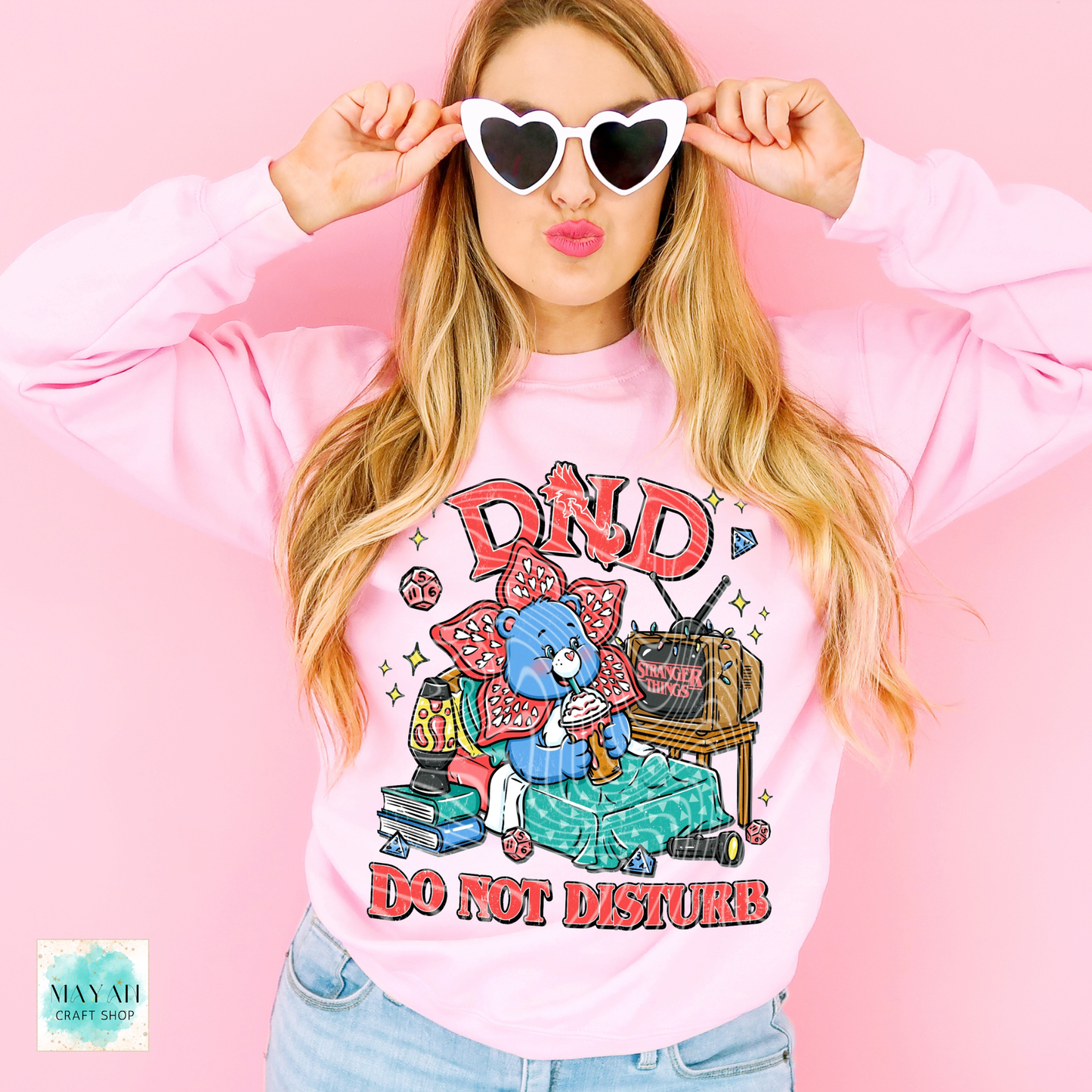 Woman wearing a pink sweatshirt with a graphic design and sunglasses, against a pink background.