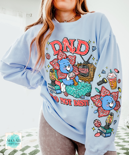 Light blue sweatshirt with colorful graphic design featuring a bear and text, worn by a person.