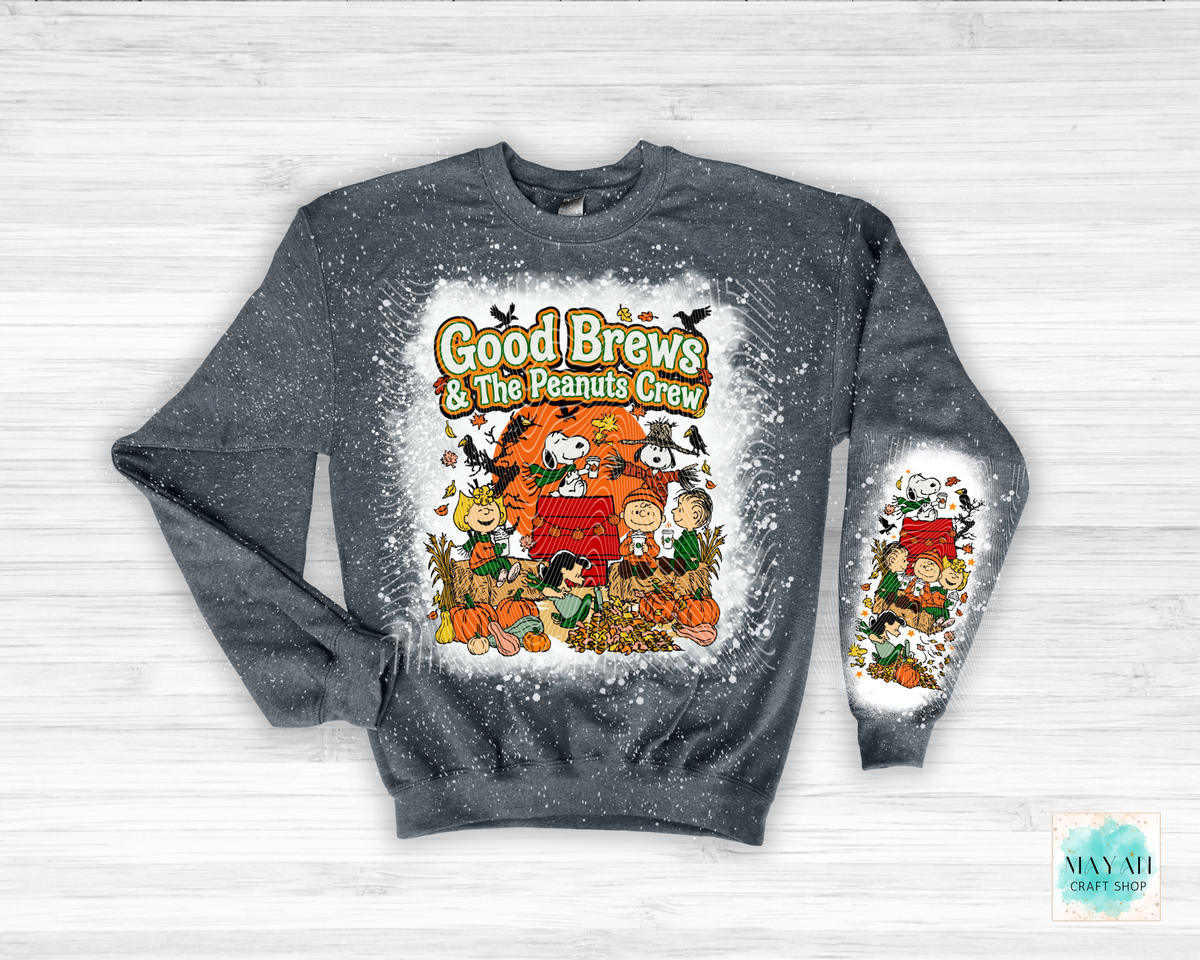 A heather charcoal crewneck sweatshirt featuring a festive 'Good Brews' graphic on the front and sleeve, displayed flat on a white wood background.