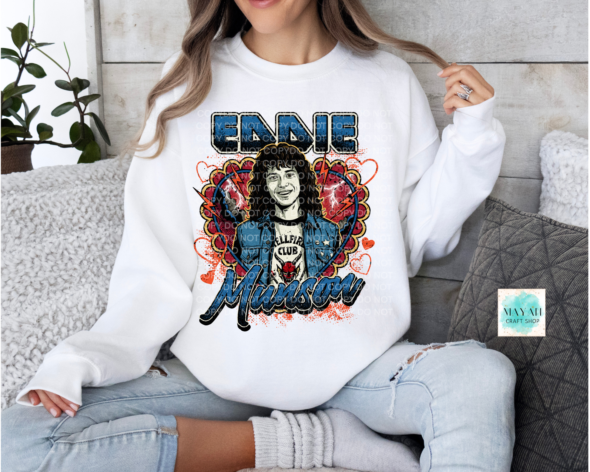 Person wearing a white sweatshirt with a graphic design of a person and text, sitting on a couch.