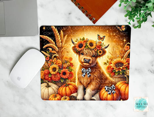 Decorative mouse pad with a highland cow wearing a flower crown surrounded by pumpkins and sunflowers on a marble surface.