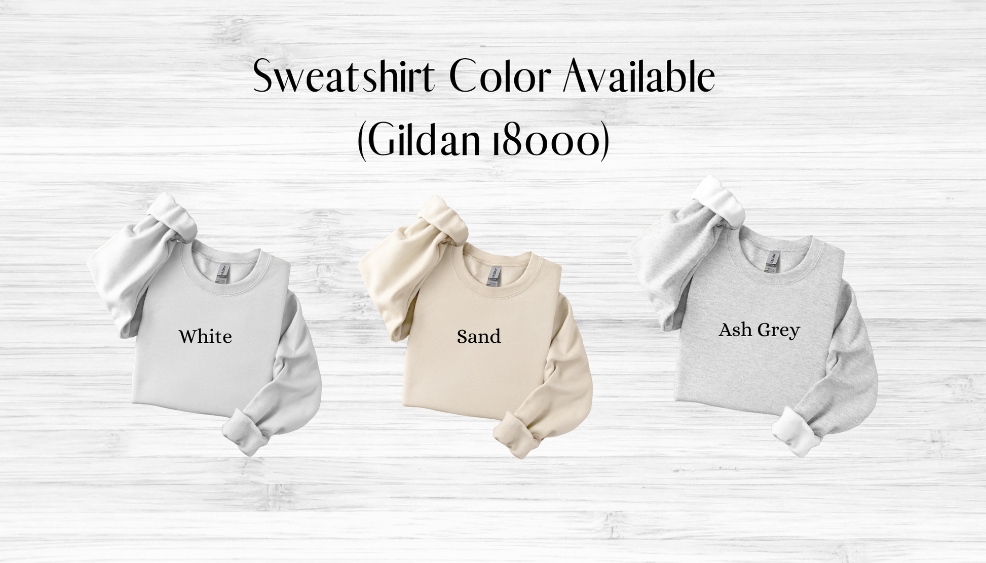 Three sweatshirts in white, sand, and ash grey with color names on a wooden surface.