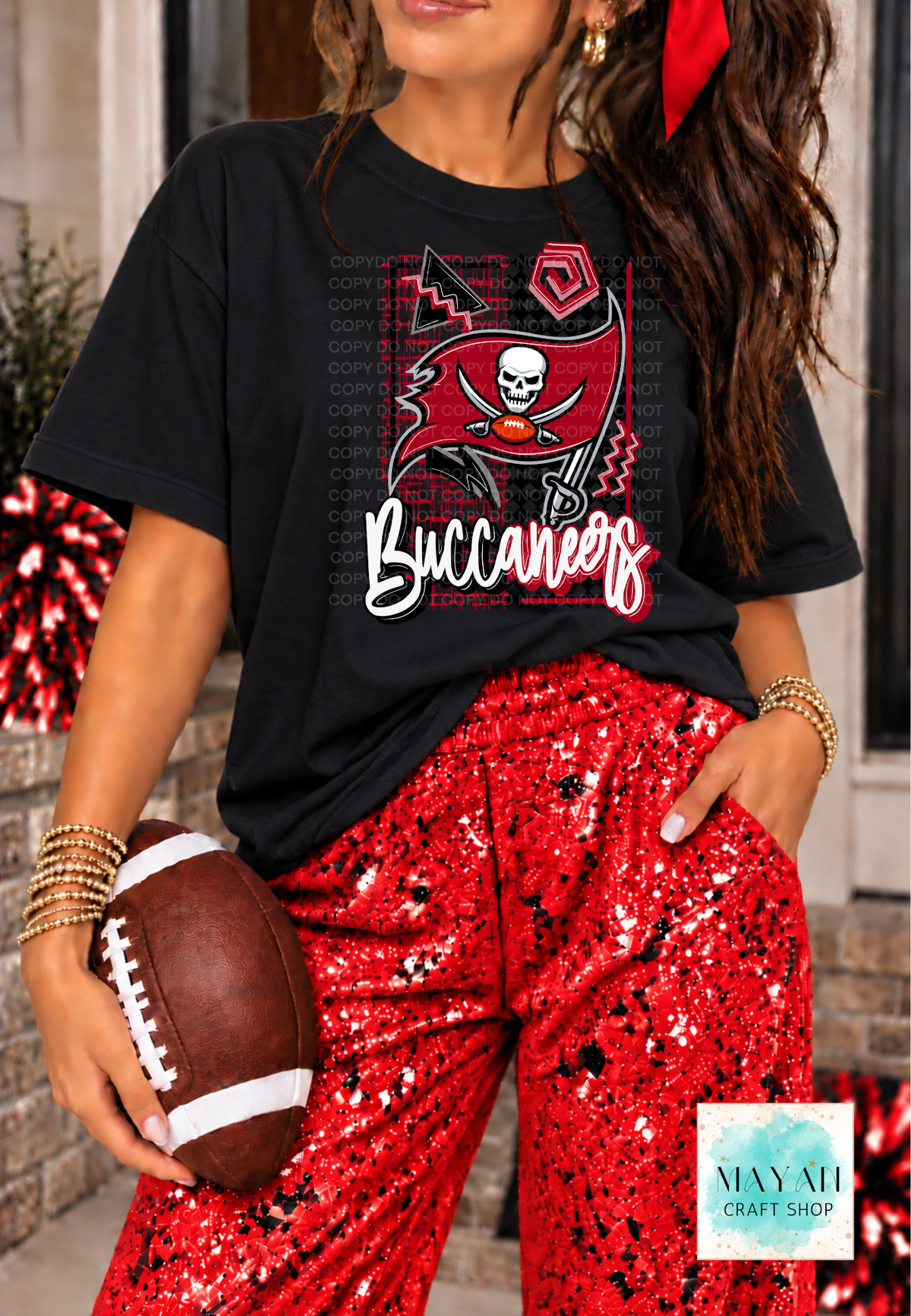 A woman wearing a black graphic T-shirt with a football team flag design and a word in white script, paired with red sequined pants, holding a football. 