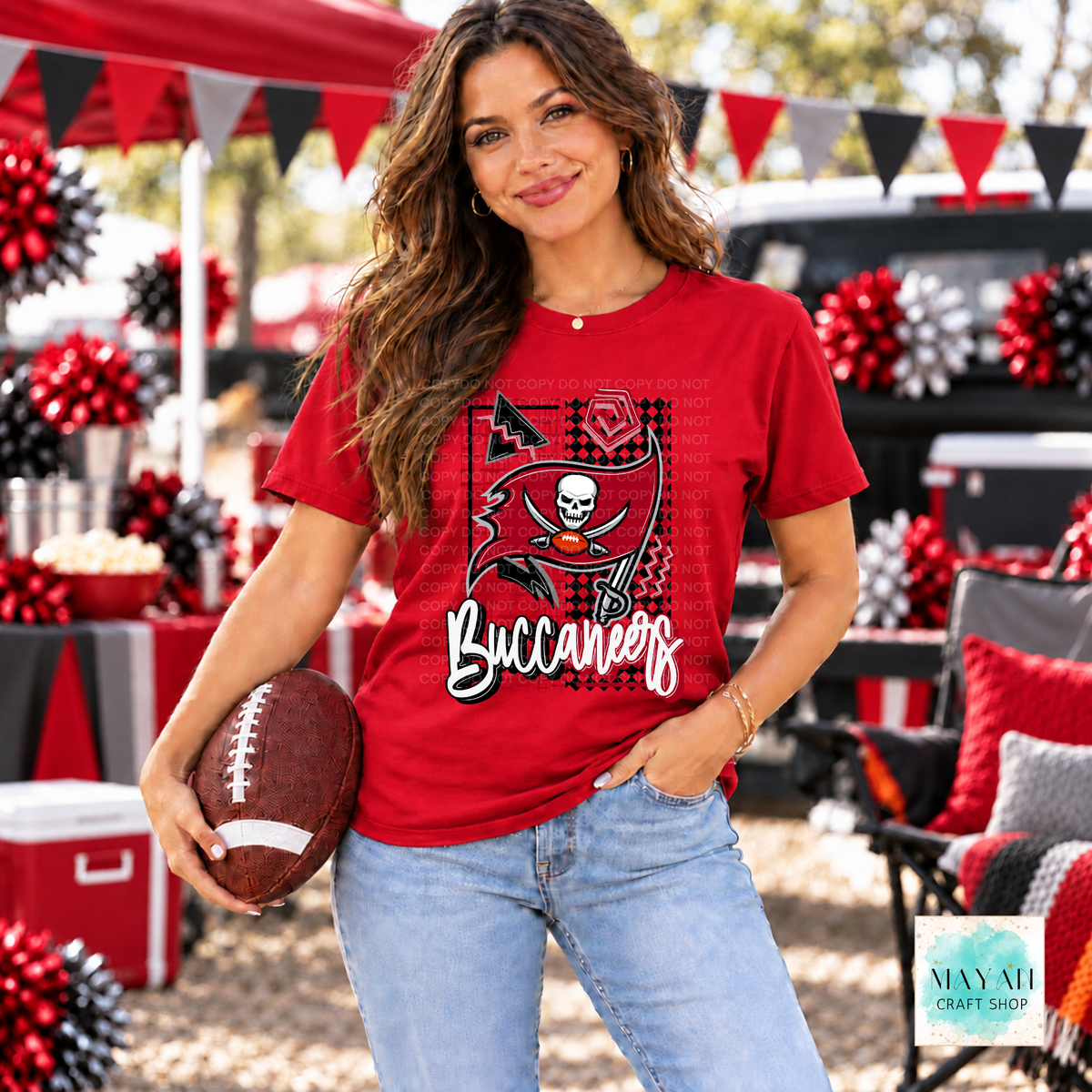 A woman wearing a red football team graphic t-shirt and light blue jeans, holding a football in an outdoor tailgate or party setting with red and black decorations.