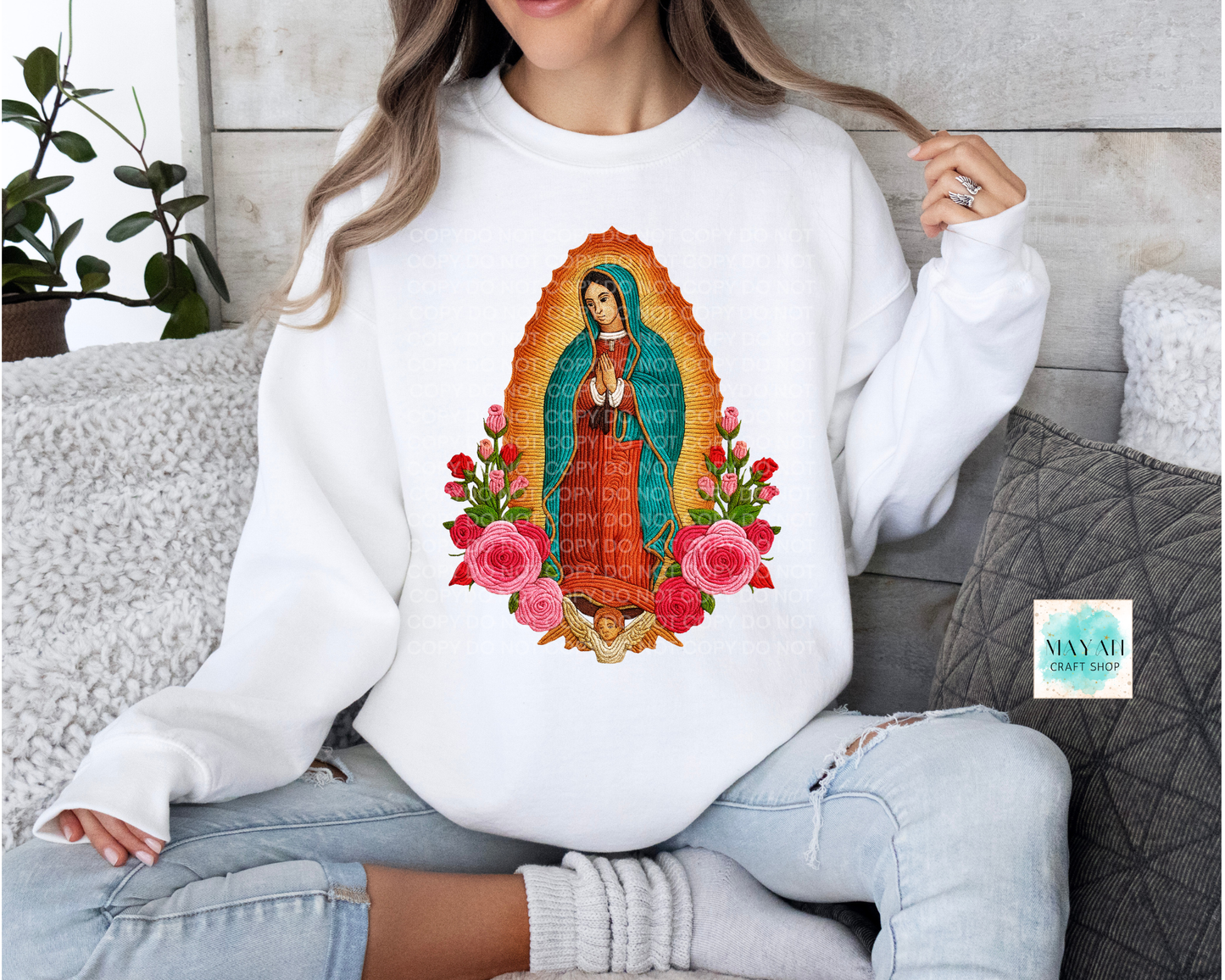 Person wearing a white sweatshirt with a colorful graphic design of Our Lady of Guadalupe and flowers.