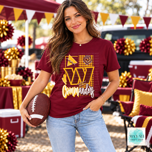 A woman wearing a maroon graphic t-shirt with a gold and yellow design, holding a football in an outdoor, decorated tailgate setting.