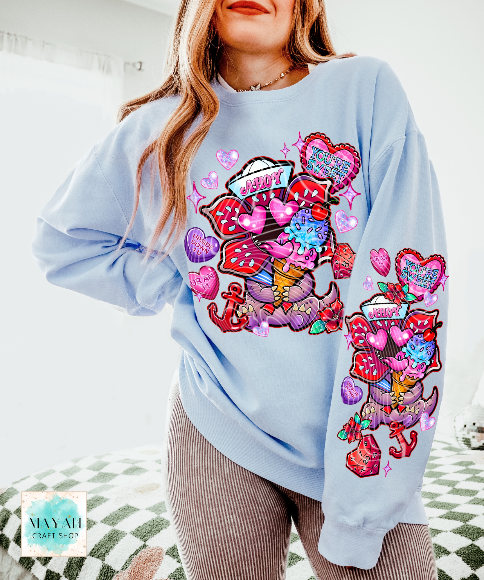 Light blue sweatshirt with colorful graphics and text worn by a person indoors.
