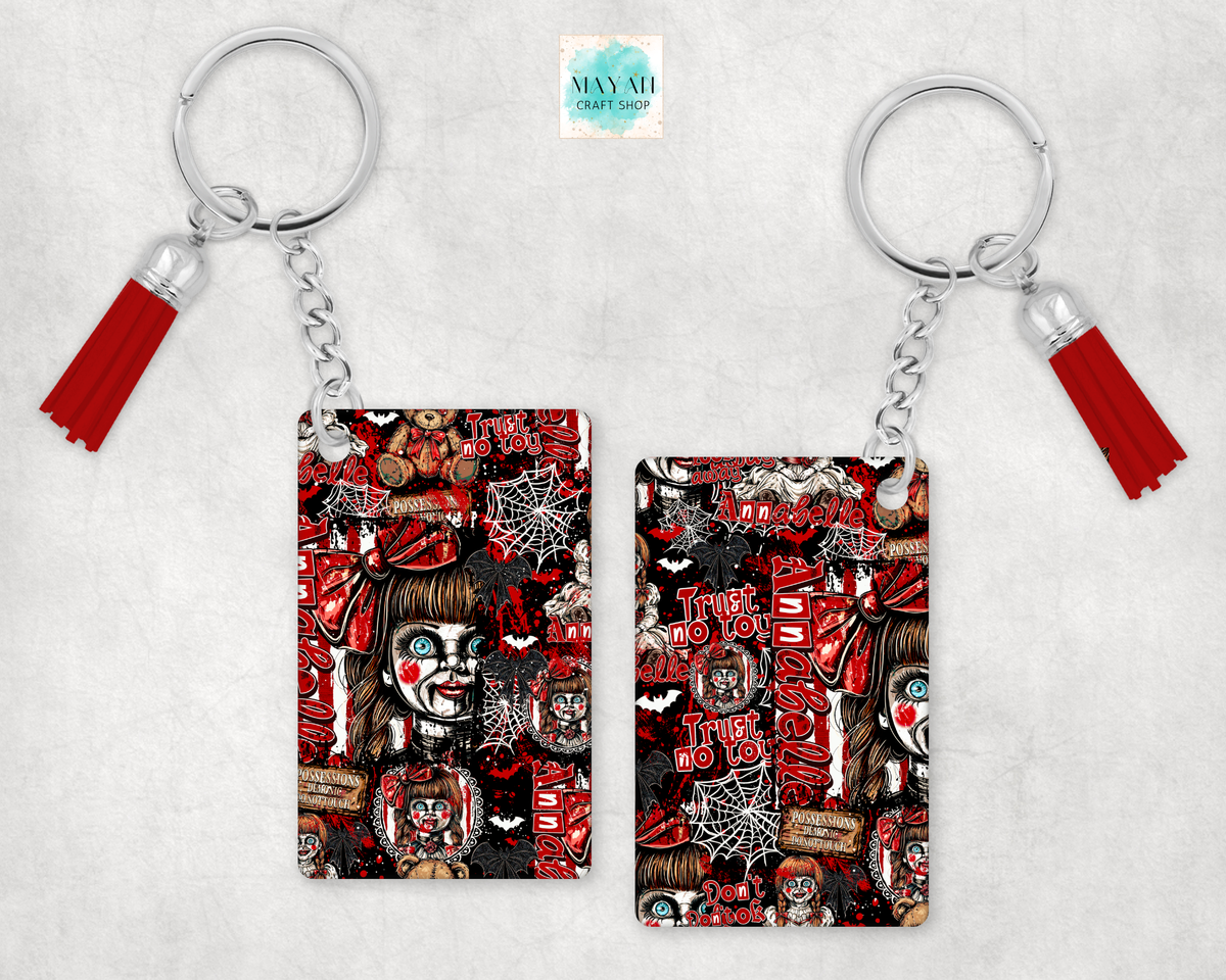 Two keychains with red tassels and silver key rings, featuring a horror-themed collage print in red, black, and white. 