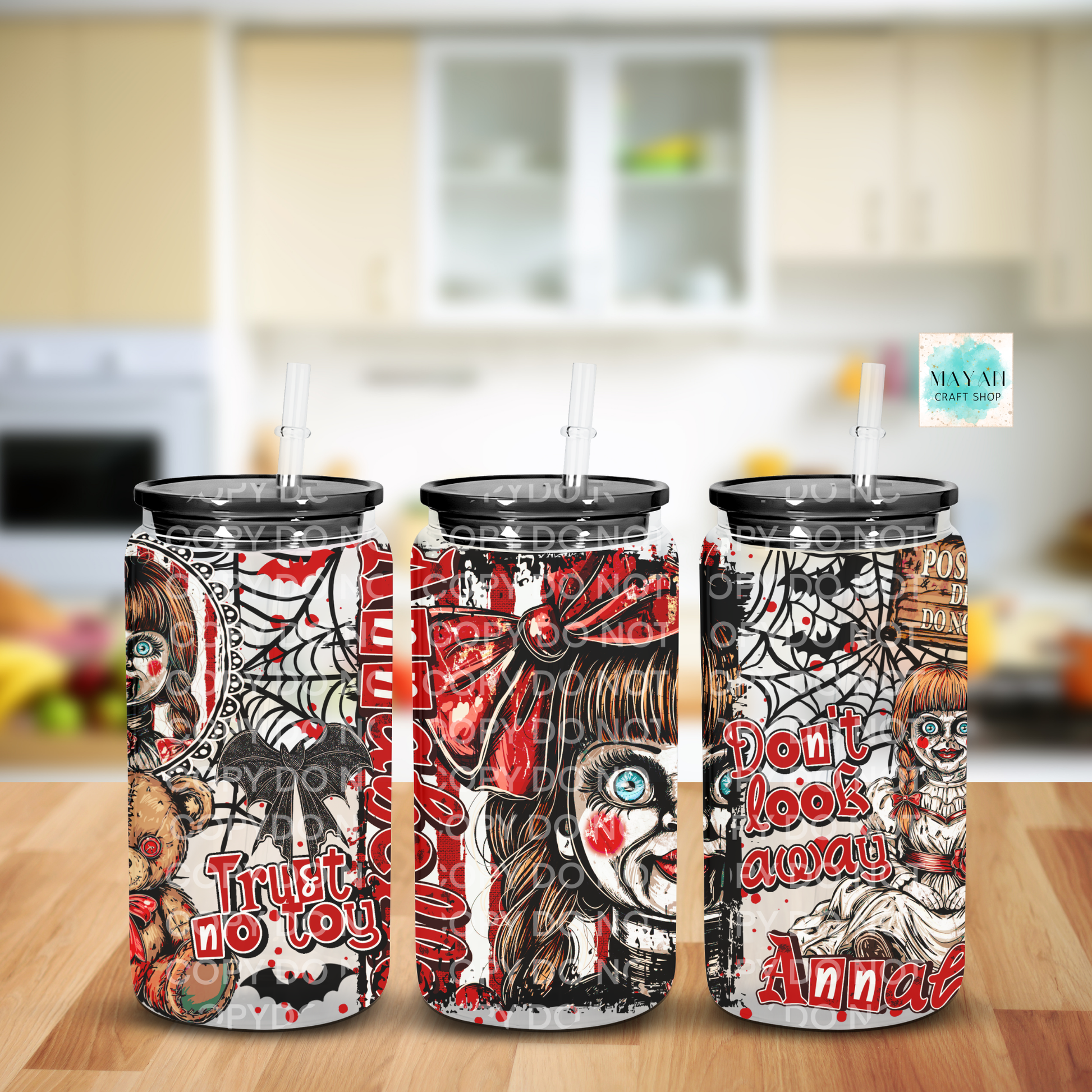 Three tall skinny tumblers with clear lids and straws, decorated with a horror-themed collage print featuring skulls, spiderwebs, blood splatters, and text including 'Trust no toy', shown on a wooden surface with a blurred kitchen background.