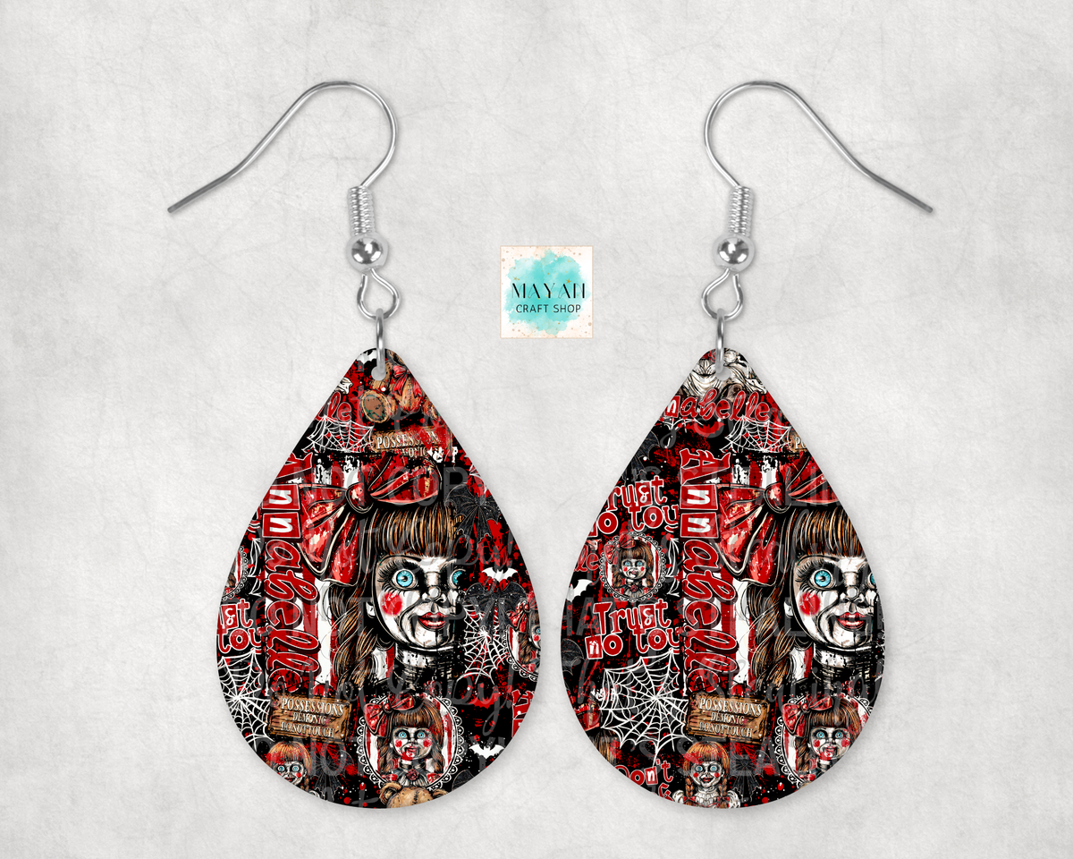 A pair of teardrop-shaped dangle earrings with silver fishhook wires, featuring a detailed horror-themed graphic print in red, black, and white. The print depicts a creepy doll face with red heart-shaped cheeks, spiderwebs, and spooky text.