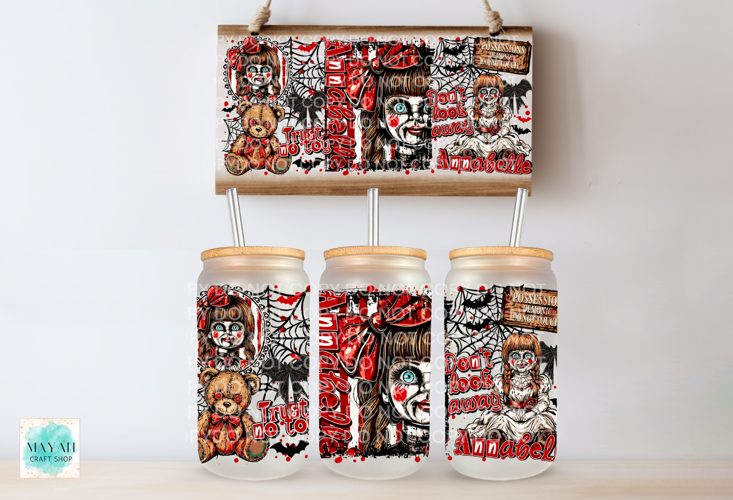 Three clear glass mason jars with light wood lids and metal straws, decorated with a spooky clown and horror-themed print, displayed below a matching rectangular print on a light wall.