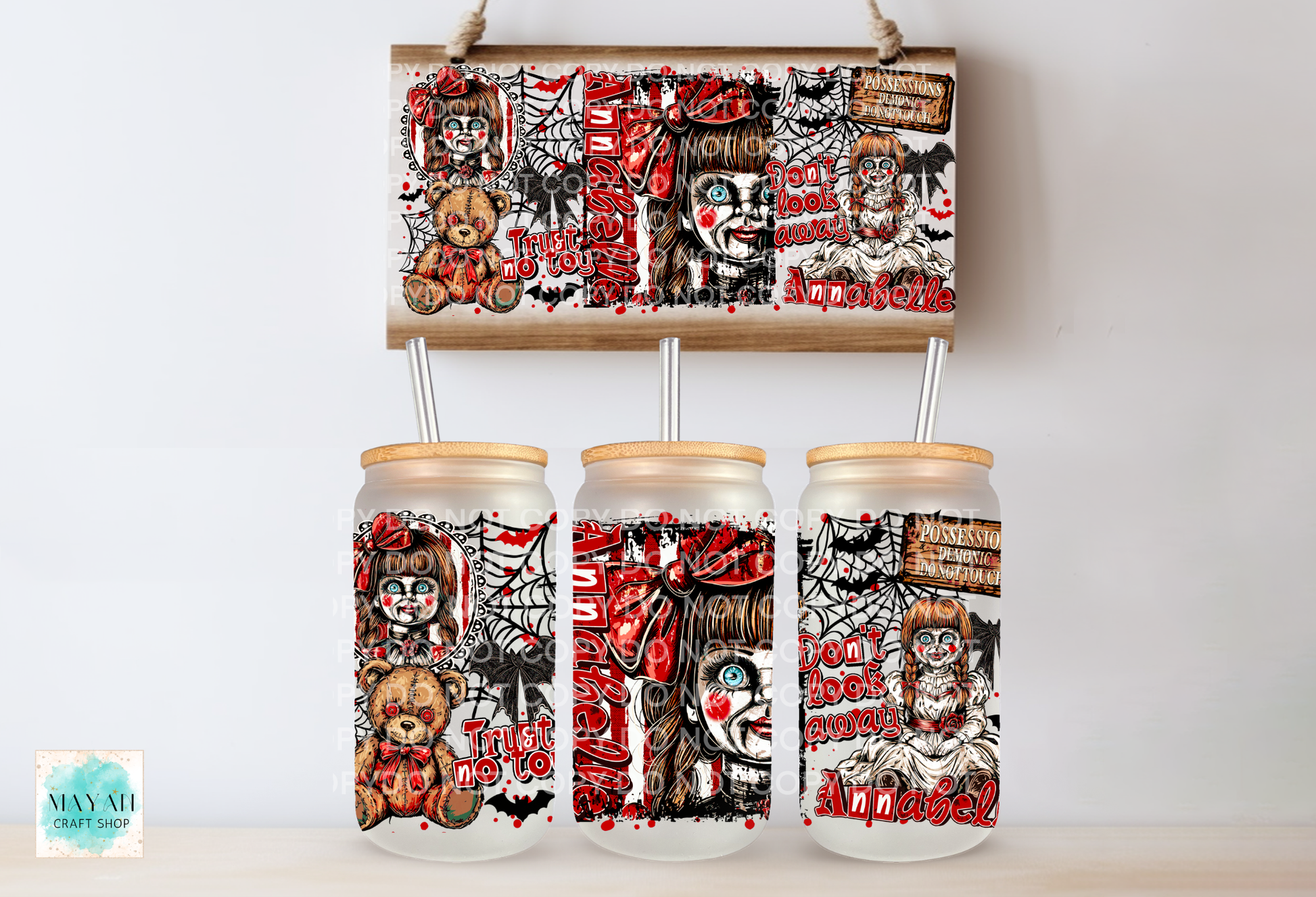 Three clear glass mason jars with light wood lids and metal straws, decorated with a spooky clown and horror-themed print, displayed below a matching rectangular print on a light wall.