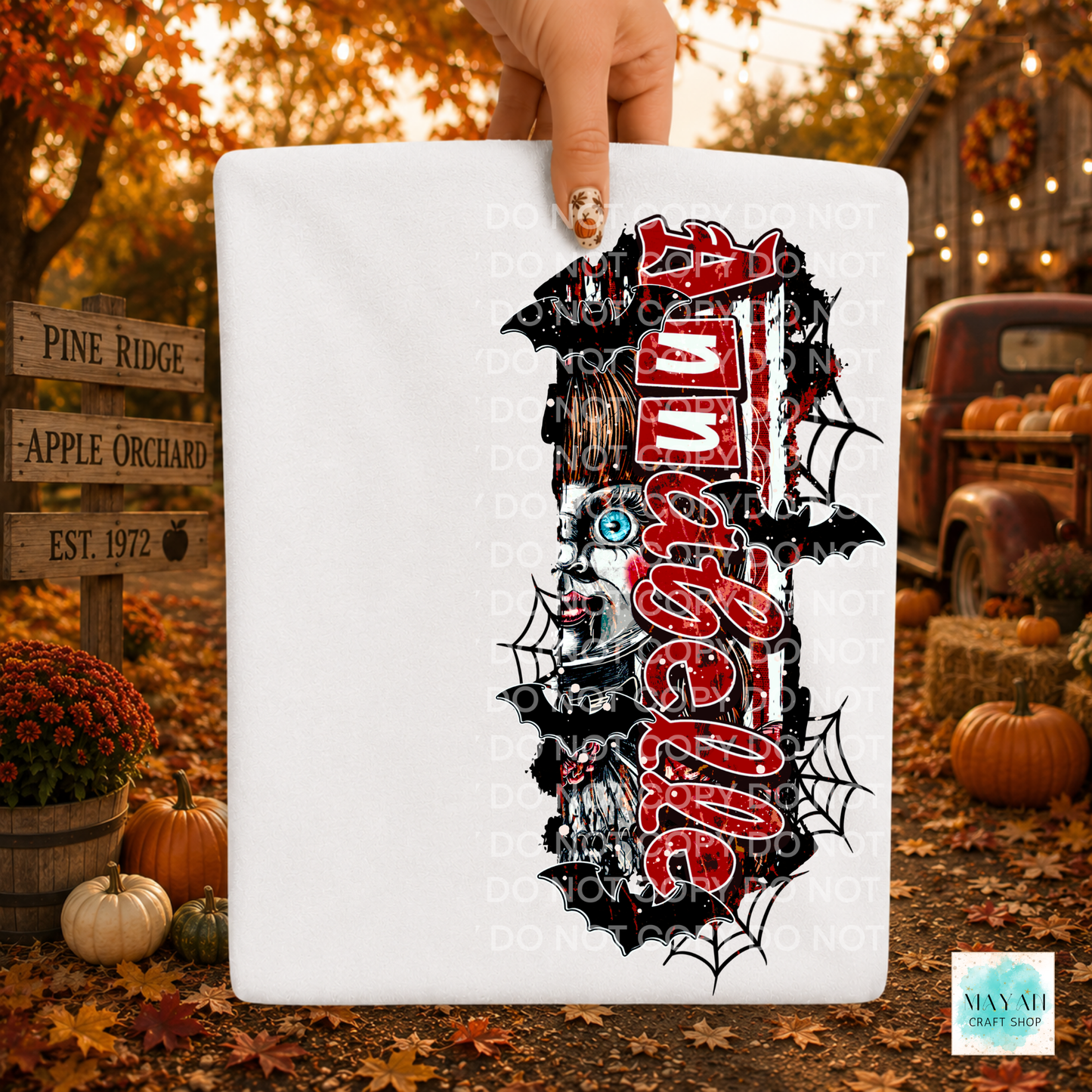A white rectangular sign or board held by a hand, featuring a large Halloween-themed graphic in red and white, bats, spiders, and a skull. The background is a fall yard scene with pumpkins, autumn leaves, and a rustic truck.