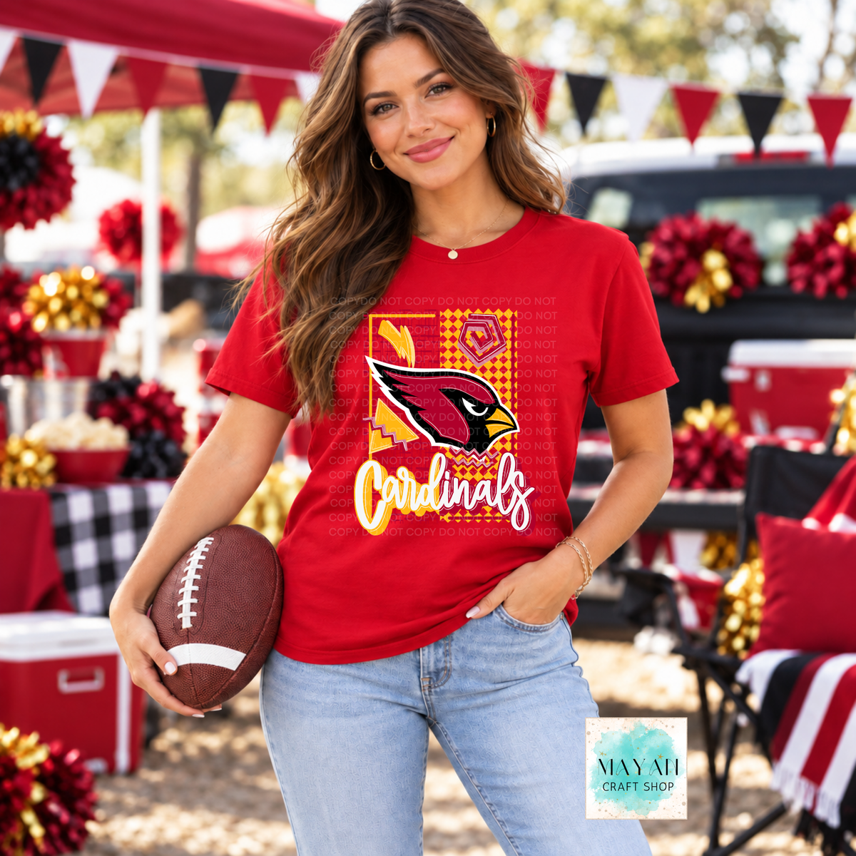 A woman modeling a red football team logo graphic t-shirt while holding a football at an outdoor tailgate or festival. The shirt features a team logo and text.