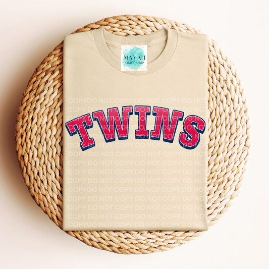Beige t-shirt with baseball logo printed in red and blue on a woven mat.