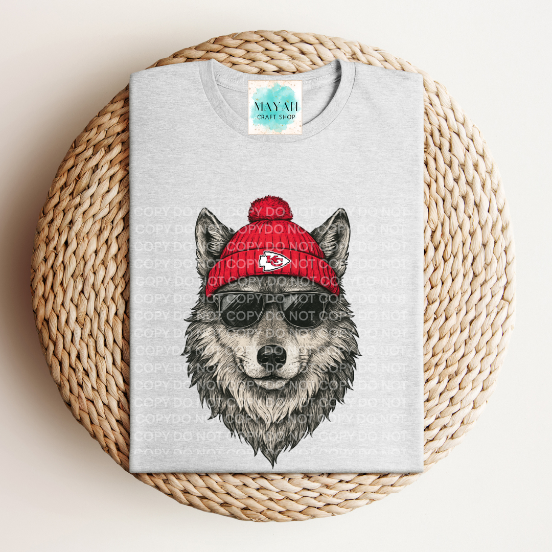 Gray t-shirt with a wolf graphic wearing a red beanie on a woven surface