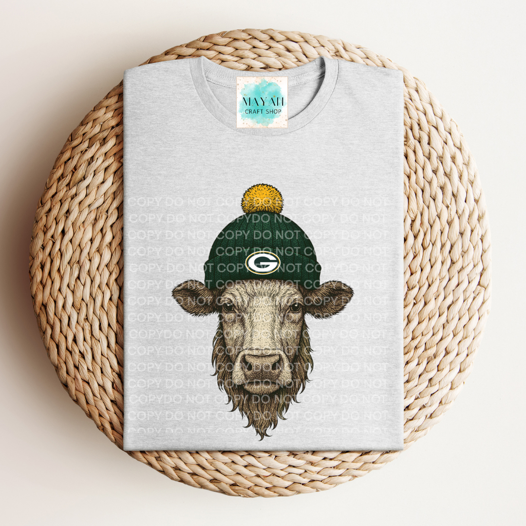 Gray t-shirt with a cow wearing a green hat on a woven mat