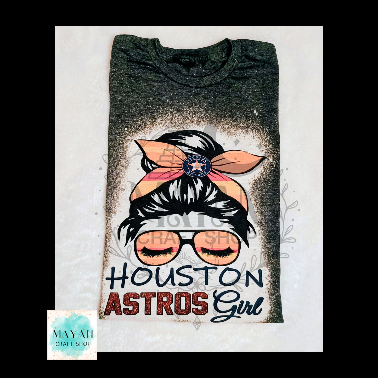 A folded dark heather gray t-shirt featuring a graphic of a woman with a pink and orange headband, glasses, and a text. The shirt is laid flat on a white textured background.