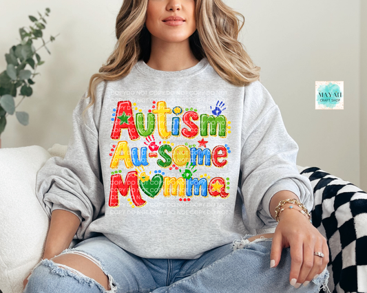Person wearing a gray sweatshirt with 'Autism Awesome Mamma' text, sitting on a couch.