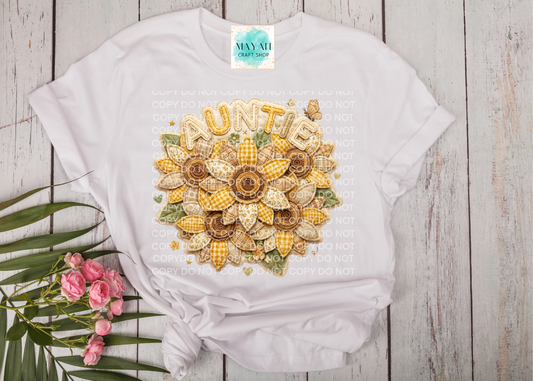 White t-shirt with a decorative sunflower design on a wooden surface with flowers and leaves.