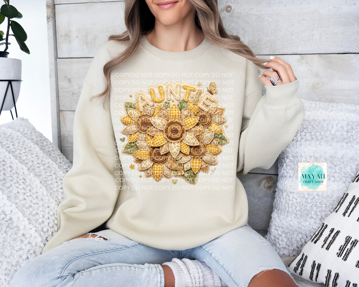 Person wearing a cream sweater with a sunflower design and 'Auntie' text, sitting on a couch.