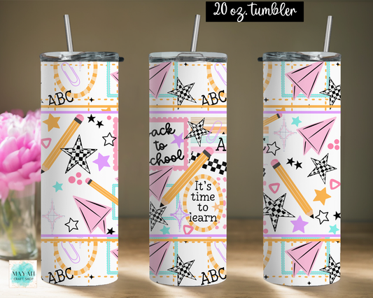 Three views of a 20 oz stainless steel tumbler with a lid and straw, featuring a colorful 'Back to School' pattern with pencils, stars, paper airplanes, and text. A pink flower vase is visible on the left, and a '20 oz tumbler' label is at the top.