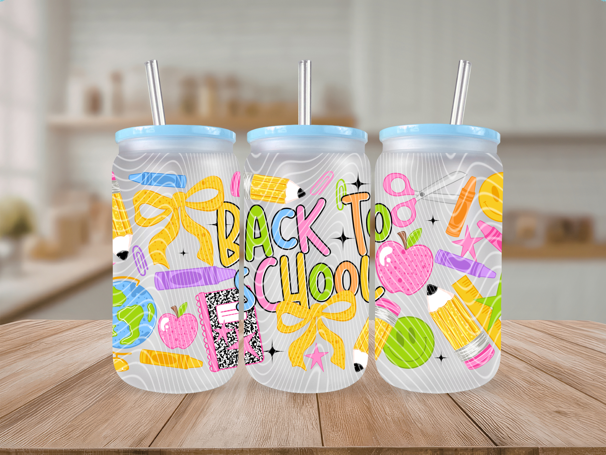 Three frosted glass cans with light blue lids and straws, decorated with colorful school-themed doodles and the words 'BACK TO SCHOOL' in pastel lettering, displayed on a wooden surface with a blurred kitchen background.