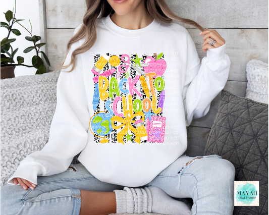 A woman wearing a white crewneck sweatshirt with a colorful 'Back to School' graphic, paired with light-wash ripped jeans and gray socks, sitting on a couch.