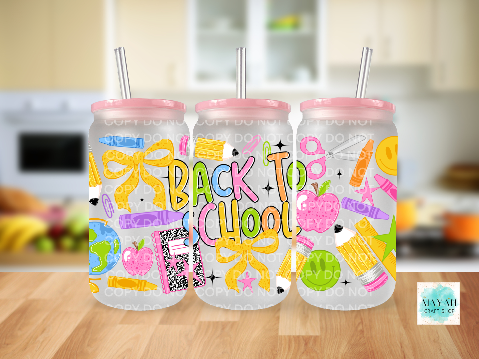 Three frosted glass cans with pink lids and metal straws, decorated with colorful school-themed graphics and the words 'BACK TO SCHOOL' in large multicolor letters. The tumblers are shown on a wooden surface with a blurred kitchen background.