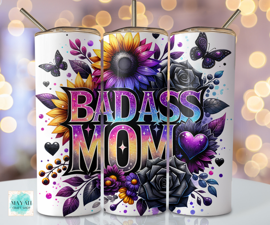 Tumbler with 'BADASS MOM' design featuring flowers and butterflies on a blurred lights background.