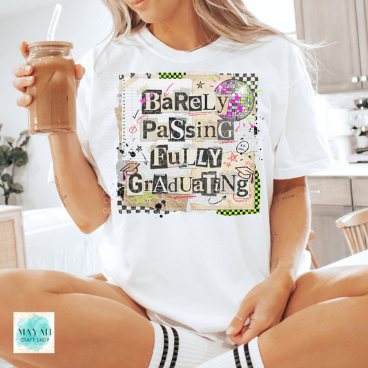 Person wearing a white t-shirt with a humorous graduation design, holding a drink.