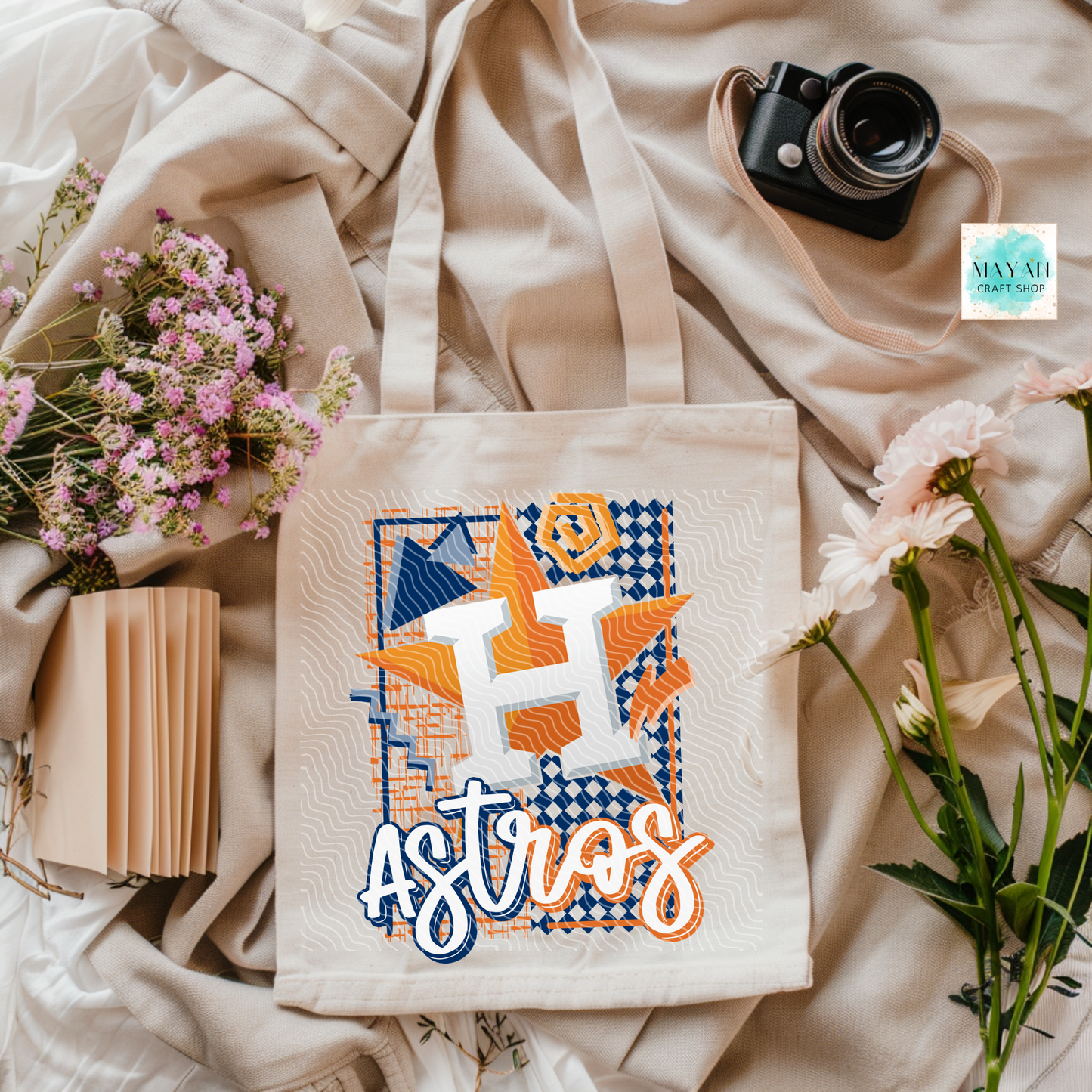Tote bag with vibrant design on a soft fabric background with flowers and a camera.