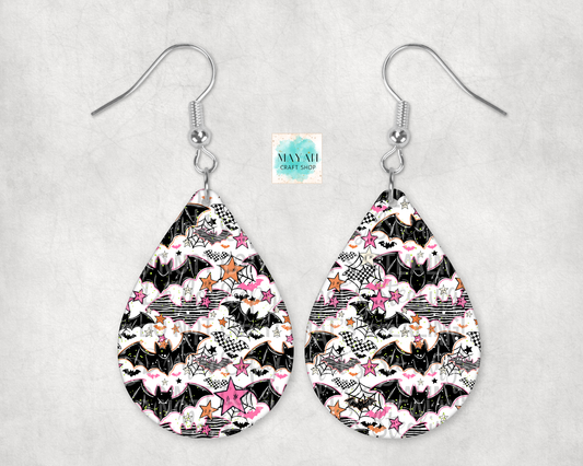A pair of teardrop-shaped dangle earrings with a black, white, and pink bat-themed pattern, hanging from silver fishhook wires on a light gray textured background.