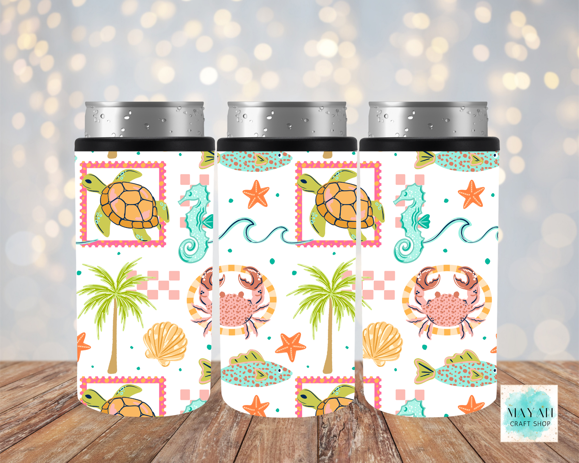 Three slim can coolers with sea-themed designs on a wooden surface.